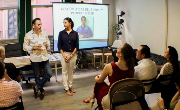 Fotografía de Gemma Ramírez en una charla sobre gestión del tiempo y productividad, junto a un presentador y frente a un grupo de asistentes en una sala de reuniones.