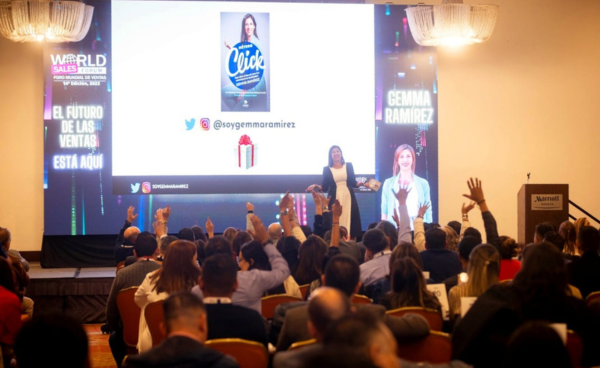 Fotografía de Gemma Ramírez presentando su libro "Click" ante una audiencia en un auditorio lleno, con pantalla gigante de fondo y asistentes participando activamente.