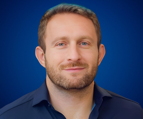 Fotografía de Andrea Iorio con camisa azul oscuro sobre fondo azul degradado, retrato profesional con expresión confiada.