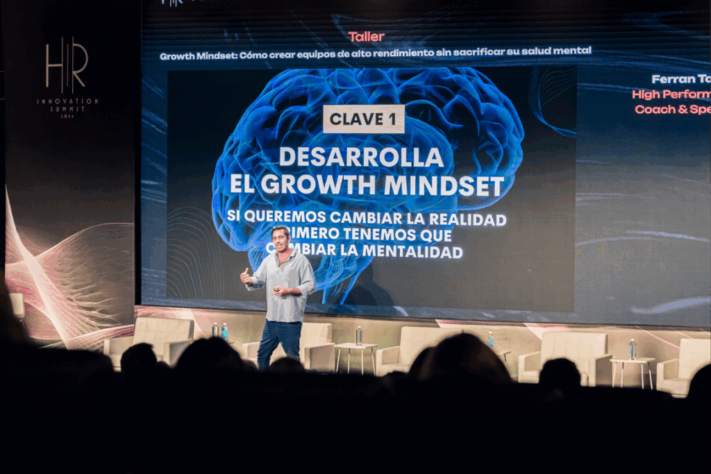 Fotografía de Ferran Tort en escena, dando una charla frente a una pantalla que despliega la frase “Desarrolla el Growth Mindset” junto a gráficos visuales.