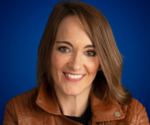 Elia Guardiola sonriendo con chaqueta de cuero marrón sobre fondo azul.