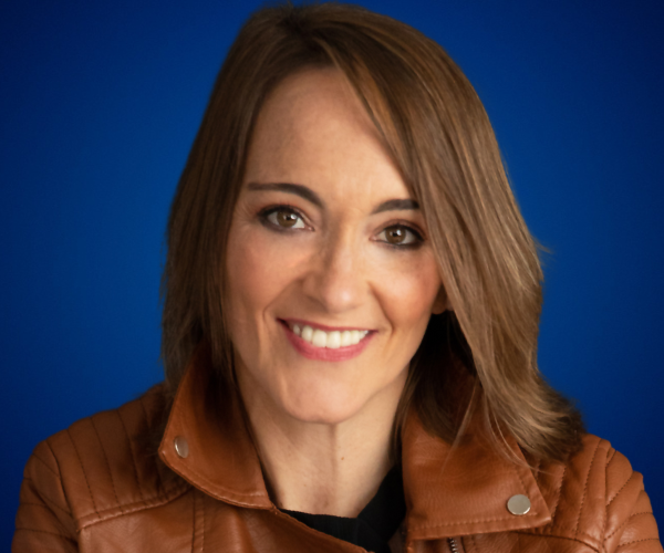 Elia Guardiola sonriendo con chaqueta de cuero marrón sobre fondo azul.