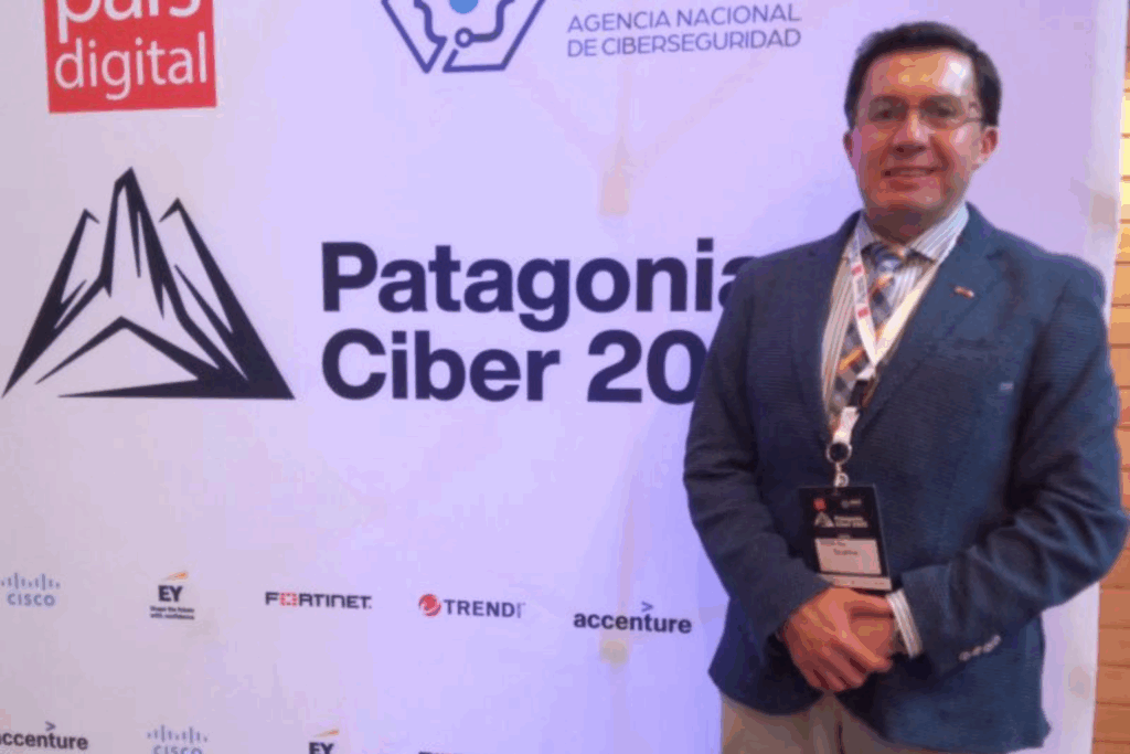 Fotografía de Rodrigo Rivera en el evento Patagonia Ciber 2023, posando con gafas y chaqueta azul frente al panel oficial del congreso de ciberseguridad.