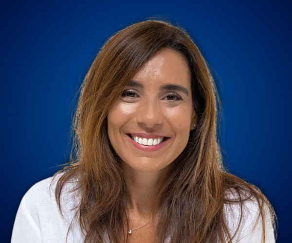 Retrato de Natalia de Vita, mujer de cabello castaño largo, sonriendo, con fondo azul.
