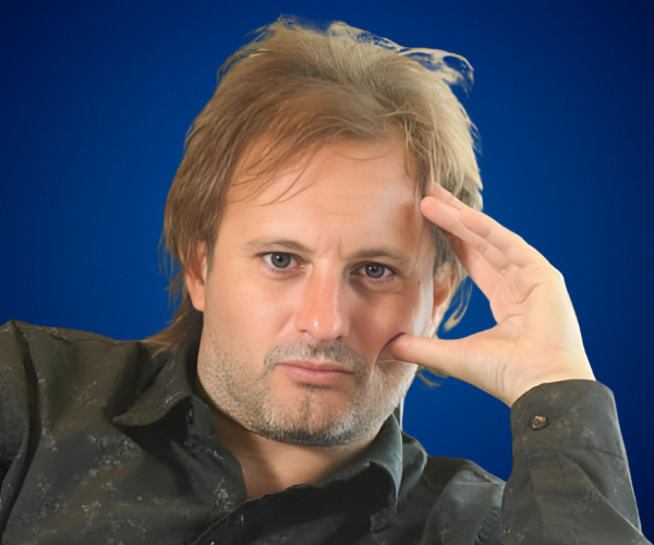 Alexis Socco, conferencista internacional, en retrato profesional con fondo azul, expresando pensamiento estratégico.