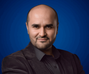 Fotografía de Fernando Veliz posando con confianza frente a un fondo azul, luciendo saco oscuro y camisa negra.