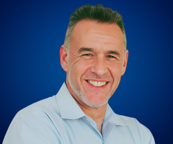 Retrato de Amikam Yalovetzky, conferencista experto en neuroventas y liderazgo, con camisa azul y fondo azul profesional.