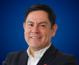 Retrato profesional de Arturo López con fondo azul, vistiendo un traje oscuro y camisa blanca, proyectando confianza y liderazgo.
