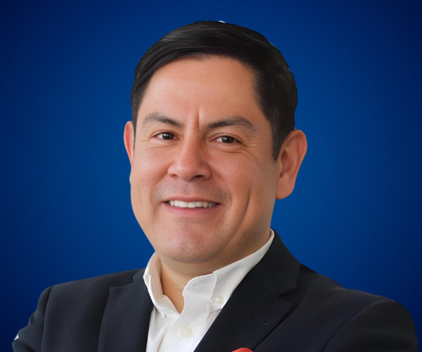 Retrato profesional de Arturo López con fondo azul, vistiendo un traje oscuro y camisa blanca, proyectando confianza y liderazgo.
