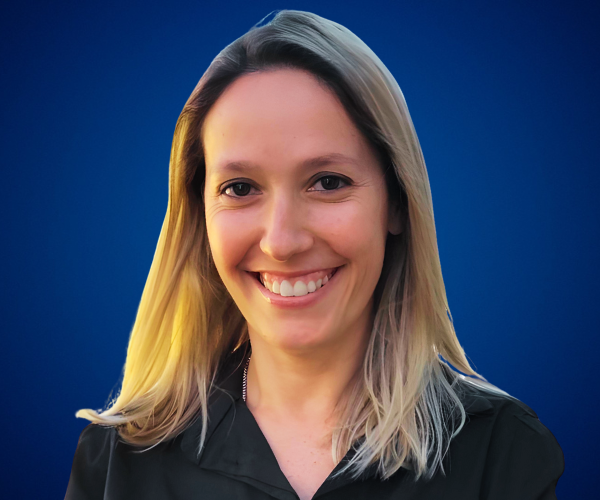Retrato de Verónica Dobronich, conferencista y coach, sonriendo con un fondo azul, vistiendo atuendo profesional.
