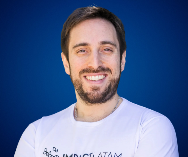 Daniel Tricarico sonriendo con camiseta blanca frente a fondo azul, experto en emprendimiento e innovación.