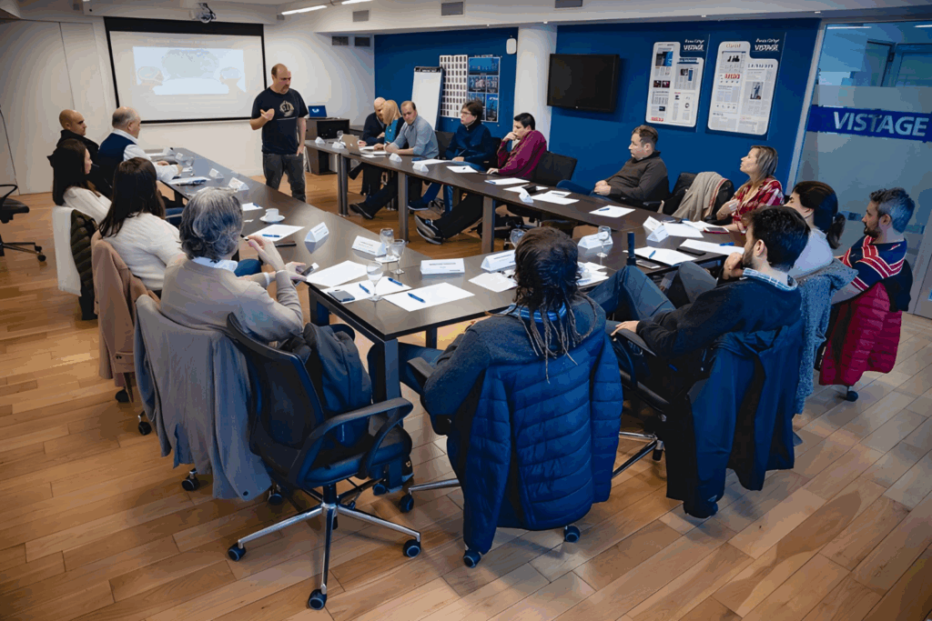 Fotografía de Pablo Nachtigall liderando una sesión de capacitación en una sala de reuniones moderna con asistentes sentados alrededor de una mesa en forma de U. Se observa una presentación proyectada y materiales de trabajo distribuidos.