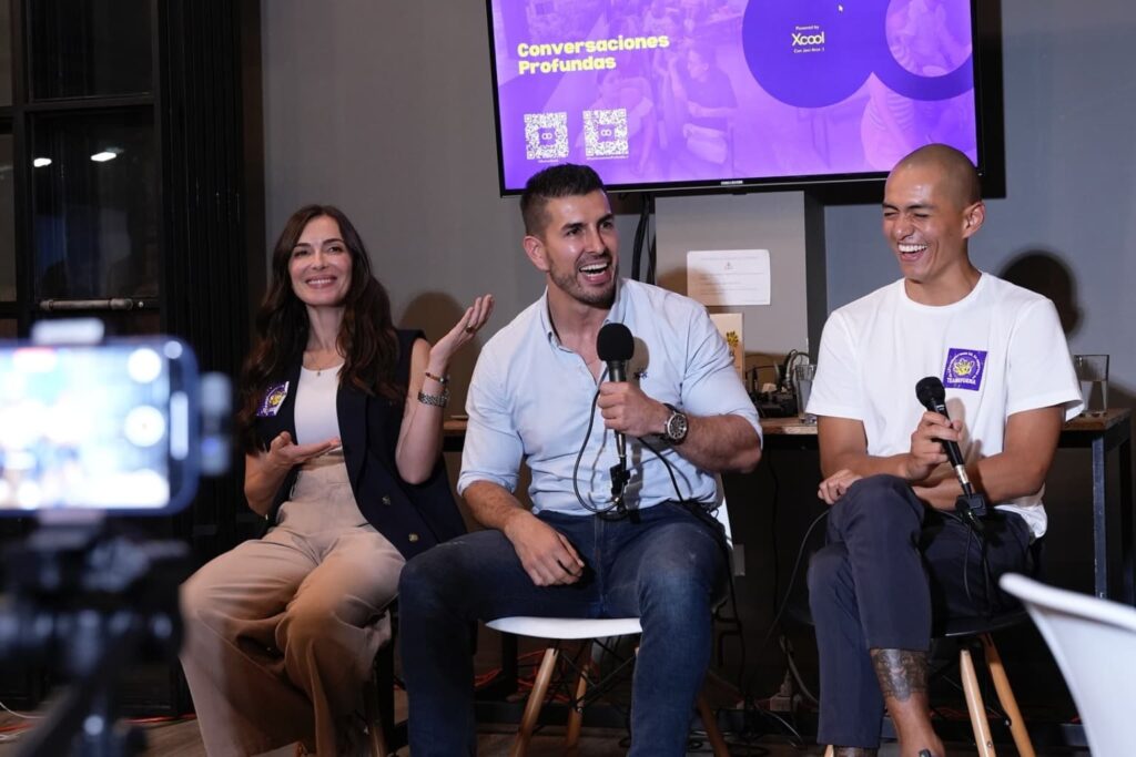 Fotografía de Catalina Serna junto a dos conferencistas, participando en un panel titulado “Conversaciones Profundas”, sonriendo y compartiendo ideas con micrófonos en mano.