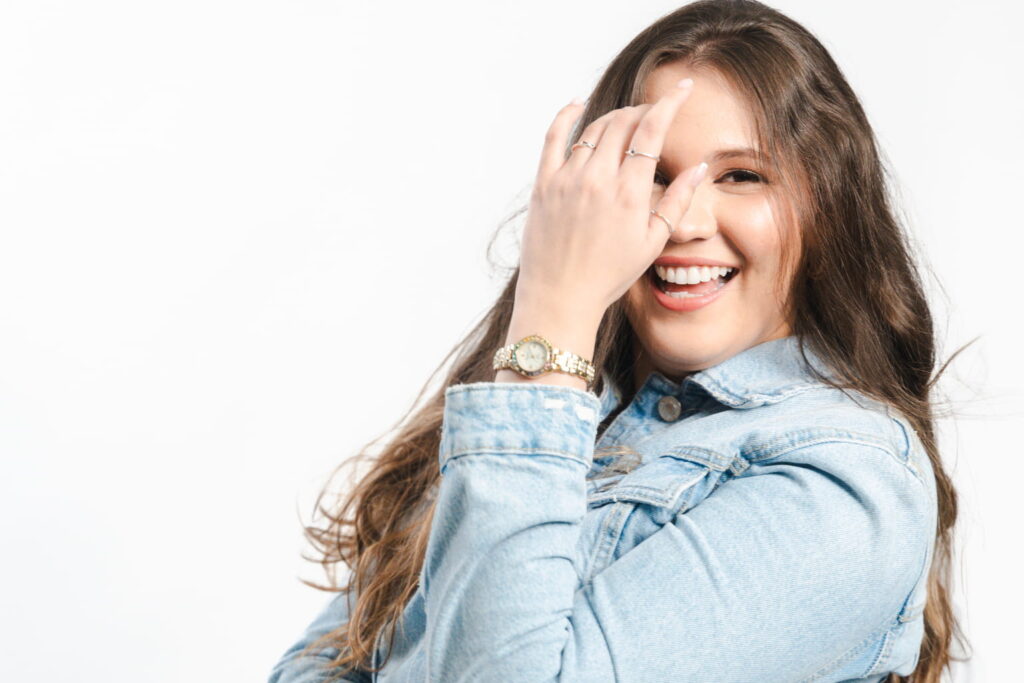 Fotografía de Danel Nouel sonriendo con expresión alegre y espontánea, vistiendo chaqueta de mezclilla y posando con confianza sobre un fondo blanco.