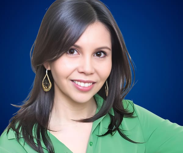 Fotografía de Pamela Lagos, con blusa verde y fondo azul, sonriendo con expresión amigable y profesional.