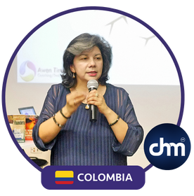 Fotografía de Lyda Ardila durante una conferencia, con micrófono en mano, blusa azul y fondo de presentación, acompañada del sello de Colombia y el logotipo de CHM.
